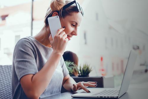 Vrouw met telefoon aan haar oor achter computer